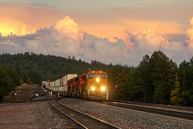 Intermodal container unit train rolls through tree-covered hills at sunset near Parks, Arizona.